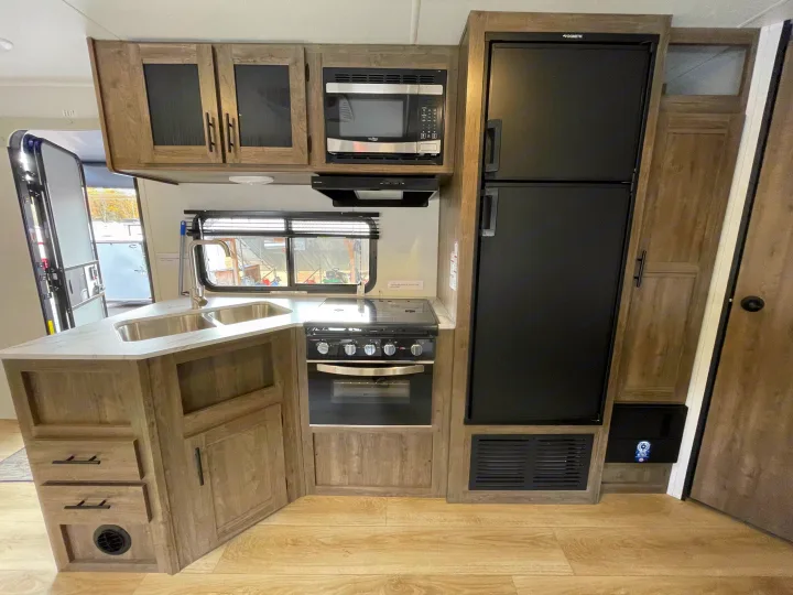 Spacious RV rental kitchen featuring a dual sink, stove, microwave, and Dometic refrigerator setup.. Heartland Pioneer 2024