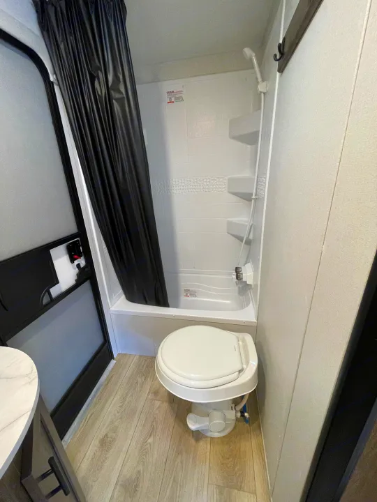 Inside an RV rental, a functional bathroom features a white shower/tub with a black curtain and a compact toilet.. Heartland Pioneer 2024