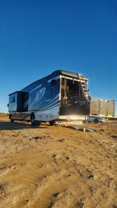 Adventure awaits with this 'Outlaw' RV rental! A toy hauler with slide-outs extended, parked on sandy ground with its rear patio open.. Thor Outlaw 2017