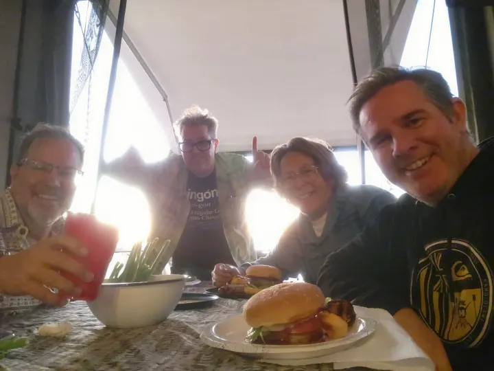 Four smiling friends enjoying burgers & drinks at a table, making memories on their rv rental adventure.. Thor Outlaw 2017