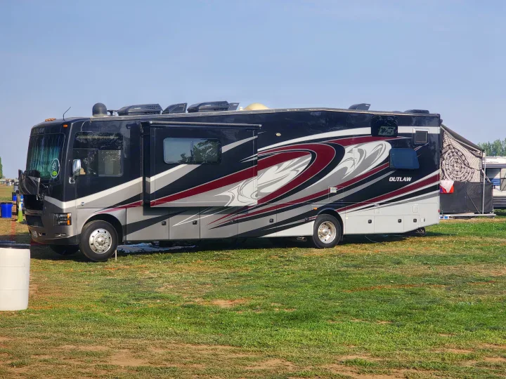 A large, black, red & grey 'OUTLAW' rv rental motorhome, with its side extended, sits on a grassy field.. Thor Outlaw 2017
