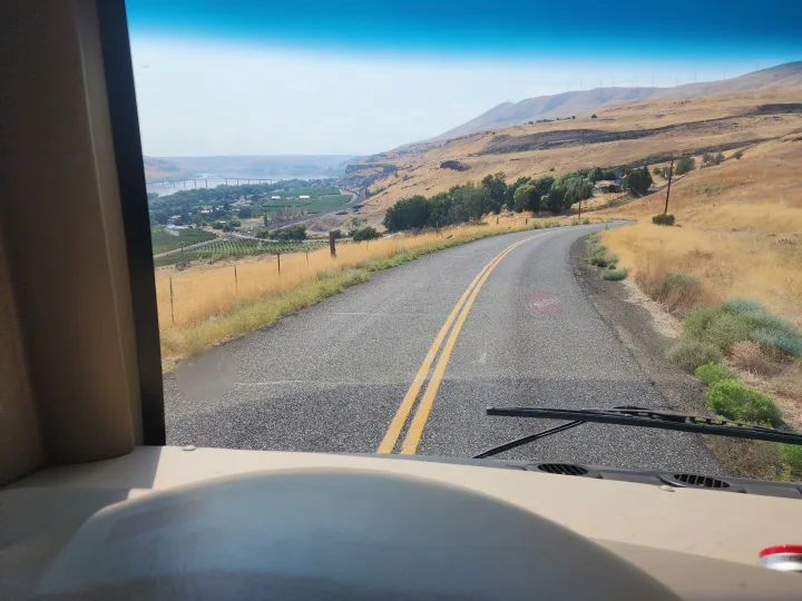 Scenic RV rental drive: winding road overlooking a valley, river, bridge, and hills with distant wind turbines.. Thor Outlaw 2017