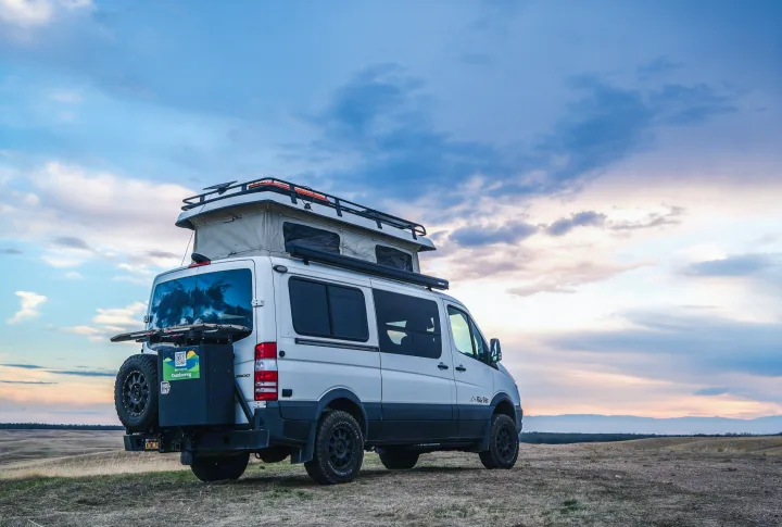This white pop-top camper van, a perfect RV rental for adventure, is parked on a scenic hill under a beautiful, cloudy sky.. Sportsmobile Regular Body 4X4 2017