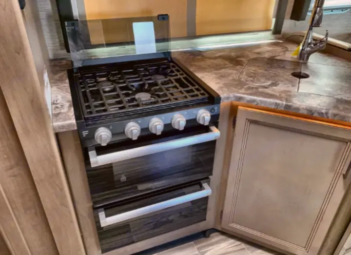 RV rental kitchen: a gas range, double oven, and speckled grey countertop with a polished chrome faucet and sink.. Thor Four Winds 2023