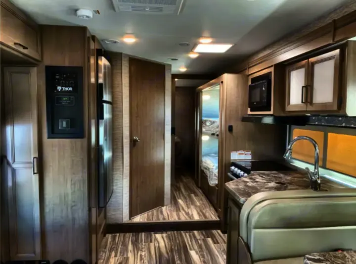 Spacious rv rental interior, featuring a kitchen with sink, stove, microwave, fridge, and dinette. A hallway leads to rear bunks.. Thor Four Winds 2023