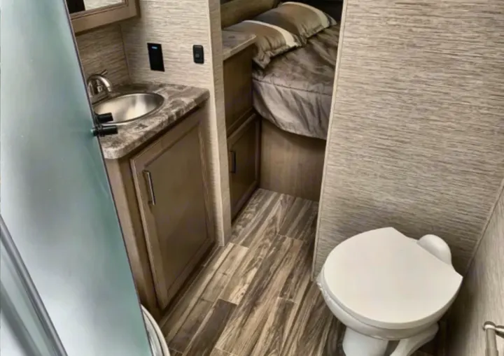 Cozy RV rental interior: compact bath with sink & toilet, seamlessly connected to a small bedroom with a bed.. Thor Four Winds 2023