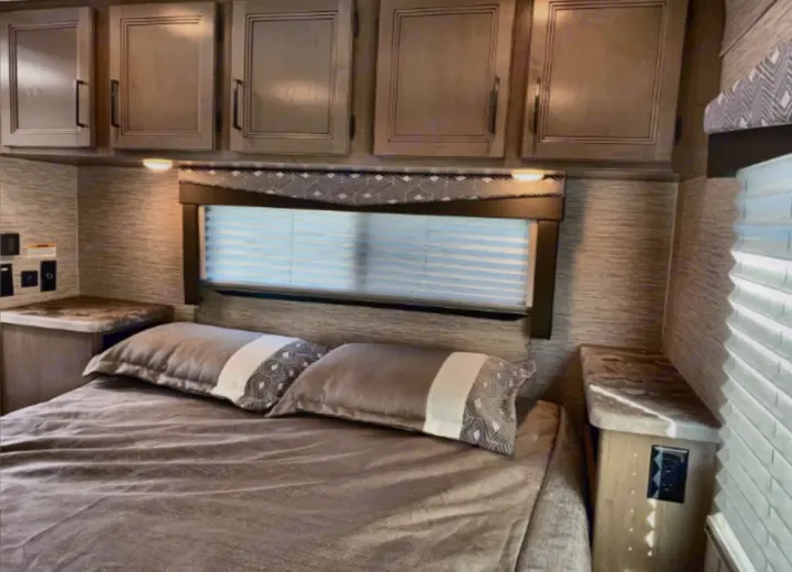 Comfortable RV rental bedroom featuring a bed, overhead storage cabinets, a window with blinds, and bedside outlets.. Thor Four Winds 2023