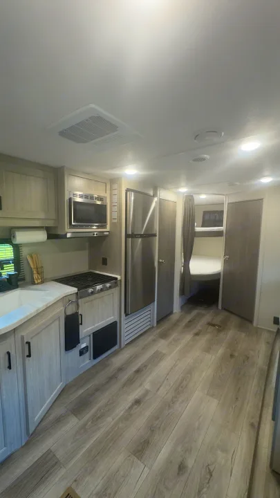 Spacious RV rental interior featuring a modern kitchen with stainless appliances, light wood flooring, and bunk beds.. Coachmen Catalina 2025