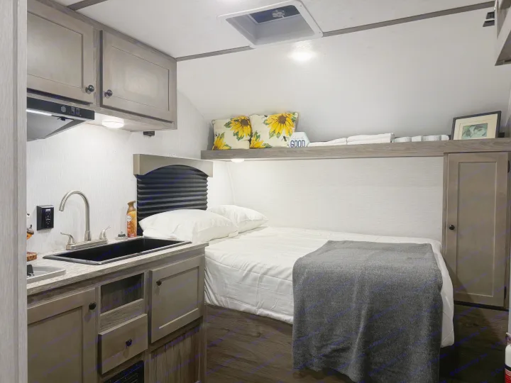 RV rental: a cozy interior featuring a bed with a grey blanket, next to a functional kitchenette with a black sink.. Sunset Park RV Sun Lite LTD 2024