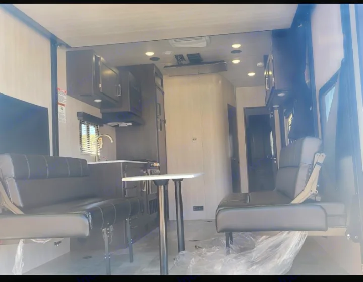 Inside an RV rental: full kitchen with microwave, sink, and two versatile black leather-look seating areas with a table.. Genesis Supreme Rv Genesis Supreme 2022