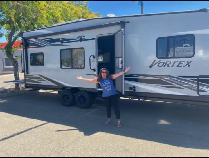 Happy woman posing with her Vortex travel trailer RV rental, ready for adventures!. Genesis Supreme Rv Genesis Supreme 2022