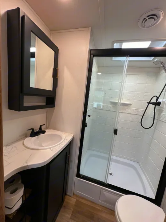 Modern & clean RV rental bathroom with a black vanity, marble counter, glass shower, and toilet, offering compact comfort.. Keystone RV Outback 2022