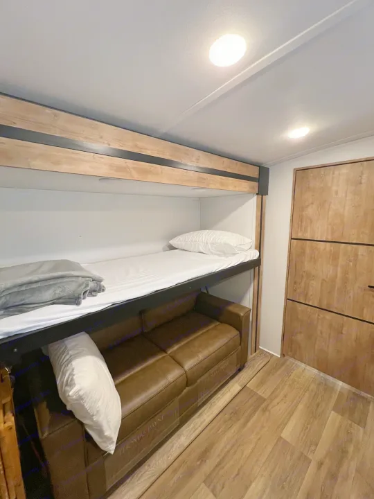 RV rental interior featuring bunk beds over a brown sofa, ideal for compact living and extra sleeping space.. Keystone RV Outback 2022