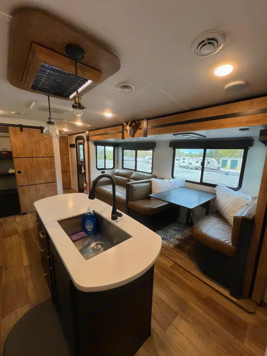 Inside a stylish RV rental: a kitchen island with a sink, brown leather seating, and a dining table. Modern design for comfortable travel.. Keystone RV Outback 2022