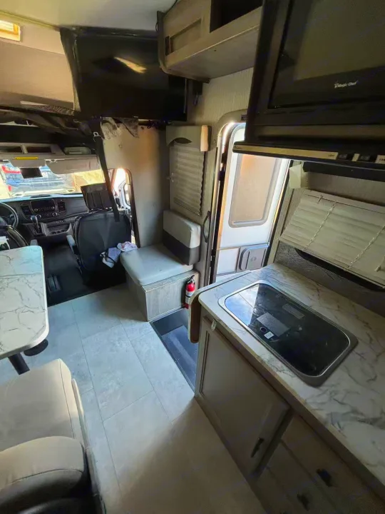 RV rental interior: kitchen with cooktop, dining table, front cabin, and overhead TV. Ideal for your next road trip adventure.. Forest River Coachmen Cross Trek 2021