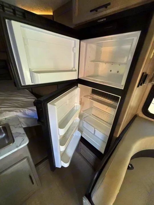Compact RV rental Dometic fridge/freezer with open doors, showcasing interior storage for your adventures.. Forest River Coachmen Cross Trek 2021