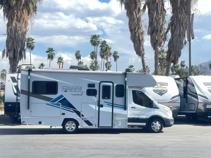Light grey Coachmen Cross Trail RV for rent, parked among palm trees. Other RVs are visible in the background.. Forest River Coachmen Cross Trek 2021