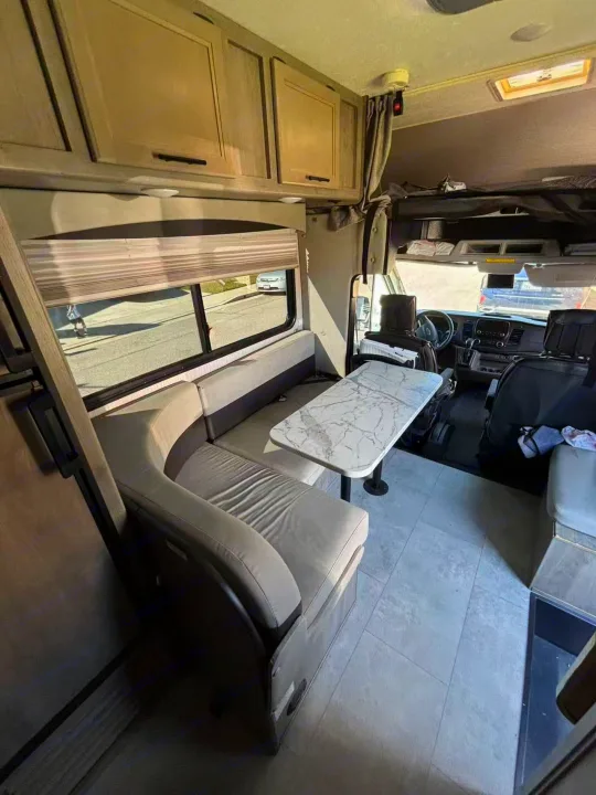 Explore this RV rental's dinette area featuring U-shaped seating, a marble table, overhead storage, and front cabin access.. Forest River Coachmen Cross Trek 2021