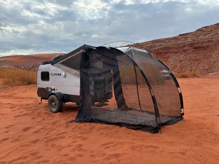 Enjoy a unique rv rental adventure! A compact travel trailer with screen room on red desert sand, rocky hills under cloudy skies.. Forest River Viking TD 2022