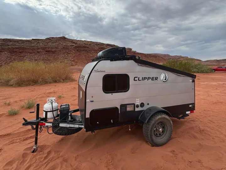 A Coachmen Clipper RV rental, equipped for off-road adventure, rests on red sand amidst towering red rock formations.. Forest River Viking TD 2022