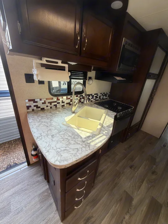 Modern RV rental kitchen featuring dark wood cabinets, a marbled countertop, sink, stove, and wood-look flooring.. Jayco Jay Flight 2018