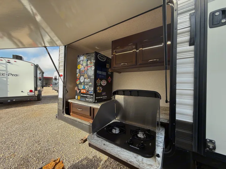An RV rental's outdoor kitchen features a sticker-covered mini-fridge, cabinets, and a Suburban stove for cooking.. Jayco Jay Flight 2018