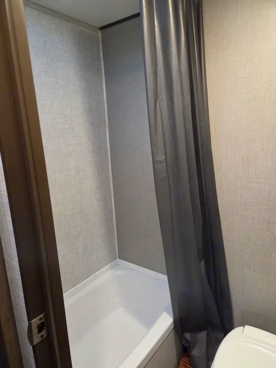 Compact RV rental bathroom with a white shower/tub, textured grey walls, and a dark shower curtain; toilet seen on the right.. Crossroads RV Zinger Lite 2021