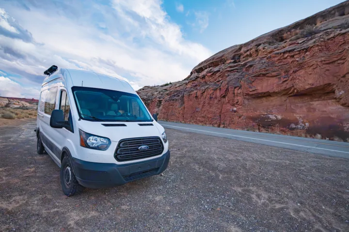 White Ford Transit camper van RV rental parked by a red rock canyon. Perfect for your next desert road trip adventure.. Ford Transit 2019