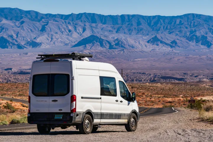 Scenic RV rental: White camper van on a desert road overlooking majestic mountains, ideal for national park exploration.. Ford Transit 2019
