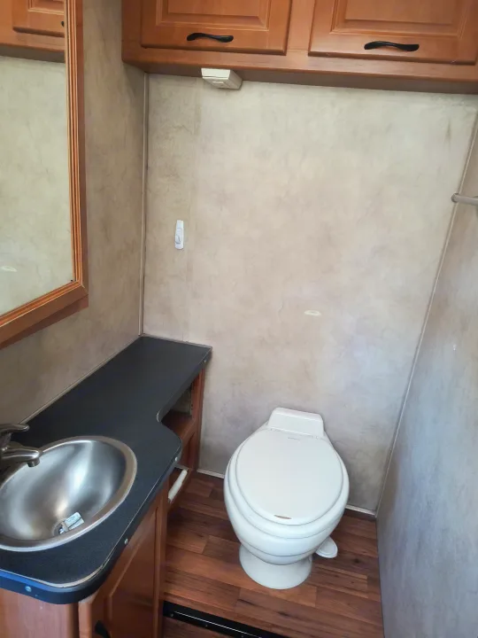 Inside an RV rental bathroom, featuring a compact toilet, vanity with sink, and mirror. Perfect for your road trip!. Thor Motor Coach Four Winds Majestic 2014