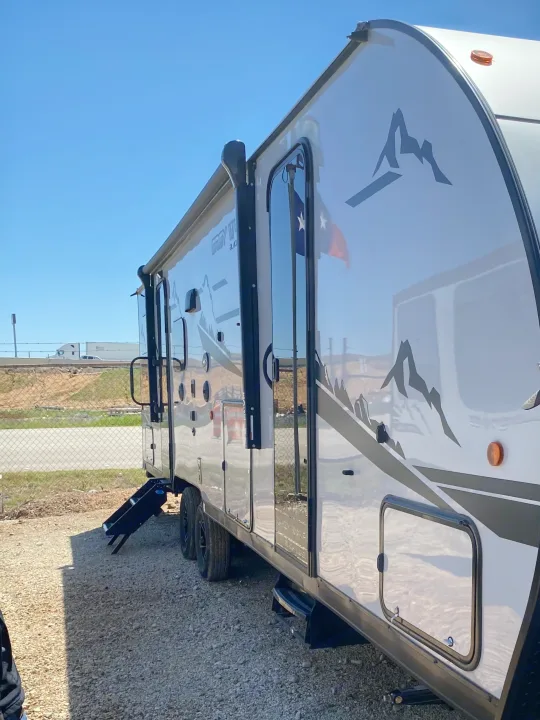 Gleaming white travel trailer RV rental with mountain graphics, showing extended steps, parked on a sunny day.. Forest River Cherokee Grey Wolf 2022