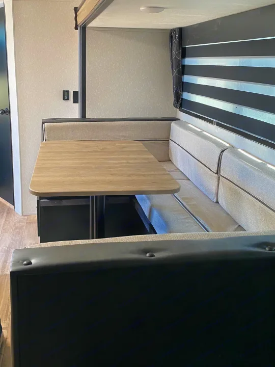 RV rental interior: cozy dinette area with light gray bench seating, wood table, and modern striped blinds.. Forest River Cherokee Grey Wolf 2022
