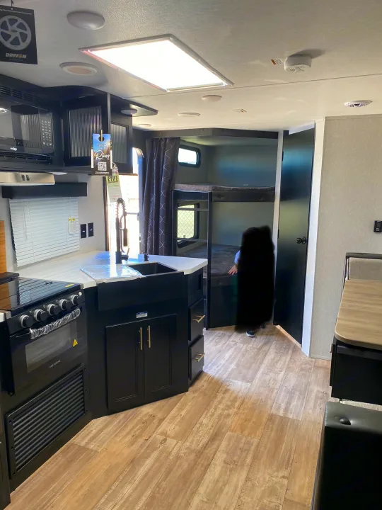 This RV rental features a modern kitchen with black cabinets, white countertops, stove, sink, and a bunk bed area.. Forest River Cherokee Grey Wolf 2022
