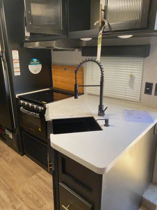 This RV rental features a modern kitchen with black Greystone appliances, white countertop, sink, and a stylish pull-down faucet.. Forest River Cherokee Grey Wolf 2022