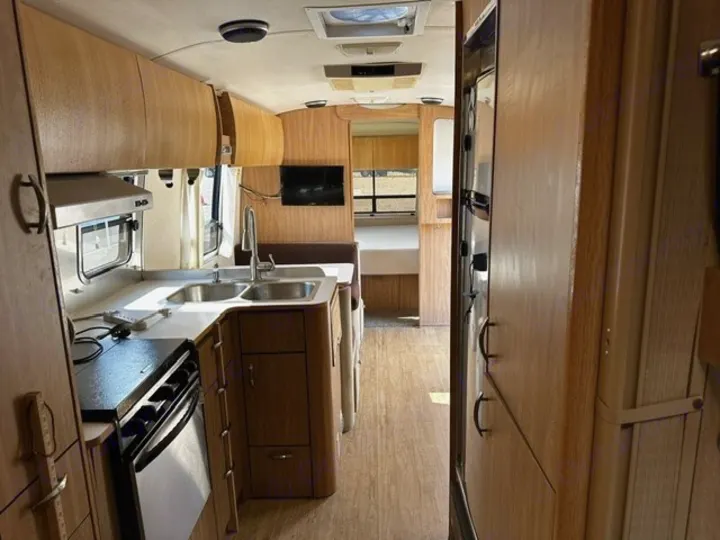 Spacious RV rental interior: equipped kitchen with sink, stove, oven, dining booth, bedroom, and ample wood cabinetry.. Airstream Safari 2006