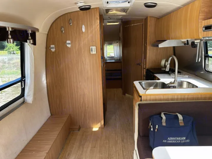 Explore this bright rv rental interior, featuring a full kitchen with sink, a cozy dinette, and warm wood-paneled walls.. Airstream Safari 2006