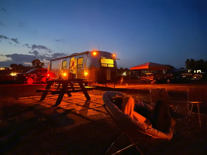 Cozy evening at a campsite: an Airstream rv rental lights up a picnic table and chairs under a twilight sky.. Airstream Safari 2006