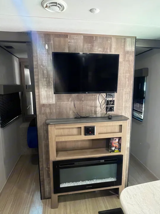 Interior view of an RV rental: features a wall-mounted TV, wood-toned entertainment center with a sleek electric fireplace.. Keystone RV Hideout 2021