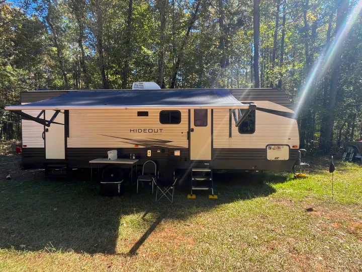 Hideout RV rental at a sunny campsite. Awning extended, with outdoor table and chairs ready for relaxation.. Keystone RV Hideout 2021