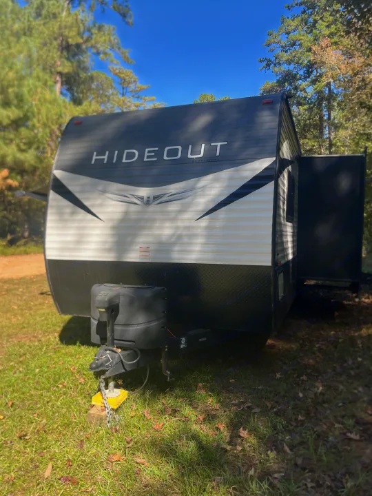 Discover this HIDEOUT by Keystone rv rental travel trailer, nestled in a grassy, wooded area under a blue sky.. Keystone RV Hideout 2021