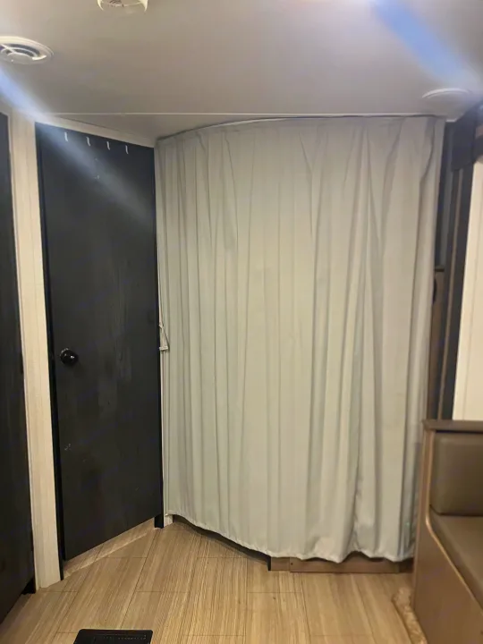 Inside an RV rental: a black door, a light gray privacy curtain, and wood-look flooring. A seating area is seen on the right.. Keystone RV Hideout 2021