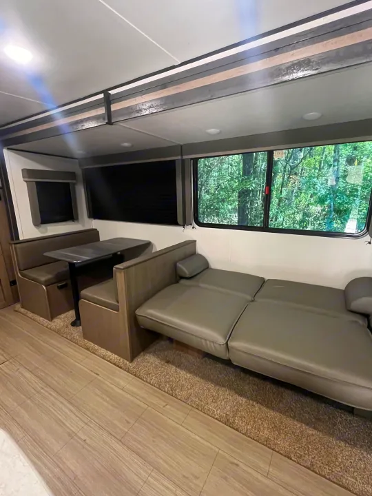 rv rental interior with comfy dinette, versatile sofa-bed, and scenic forest views through the windows.. Keystone RV Hideout 2021