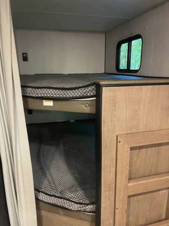 Compact RV rental bunk beds, with a window and privacy curtain, framed by light wood cabinetry for sleeping.. Keystone RV Hideout 2021