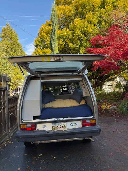 An RV rental – a silver camper van with its tailgate open to reveal a bed, nestled among vibrant autumn trees. Ready for travel.. Volkswagen T3 Westfalia 1991