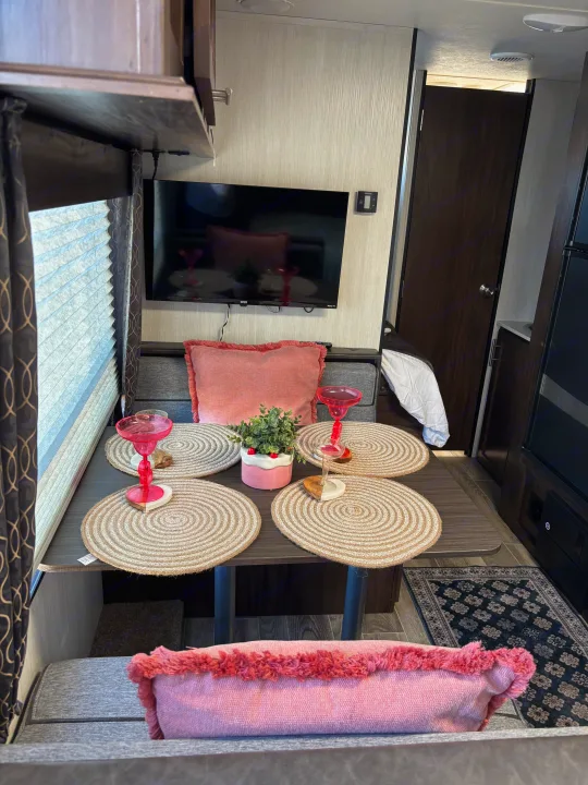Cozy RV rental dinette featuring a table set with pink decor, placemats, a wall-mounted TV, and bench seating.. Forest River Cherokee 2019