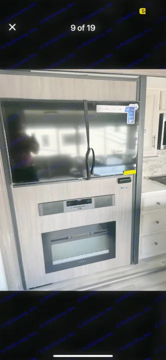 Modern RV rental interior with a wall-mounted TV, soundbar, and electric fireplace. Kitchen area visible on the right.. Forest River Sandpiper 2024