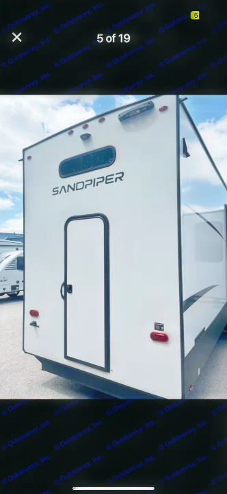 Rear view of a clean, white Sandpiper travel trailer, featuring a back door, window, and lights. Perfect for an rv rental.. Forest River Sandpiper 2024