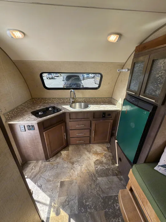 RV rental interior: A compact kitchenette with stove, sink, and fridge. Features light countertops, wooden cabinets, tiled floor, and a window view.. R-Pod Hood River Edition 2015