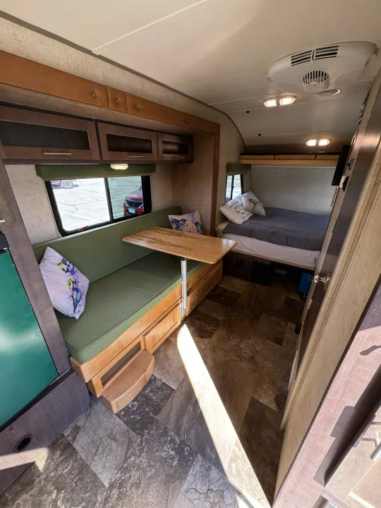 An rv rental interior featuring a dinette with green cushions, wooden table, bed, and overhead storage.. R-Pod Hood River Edition 2015