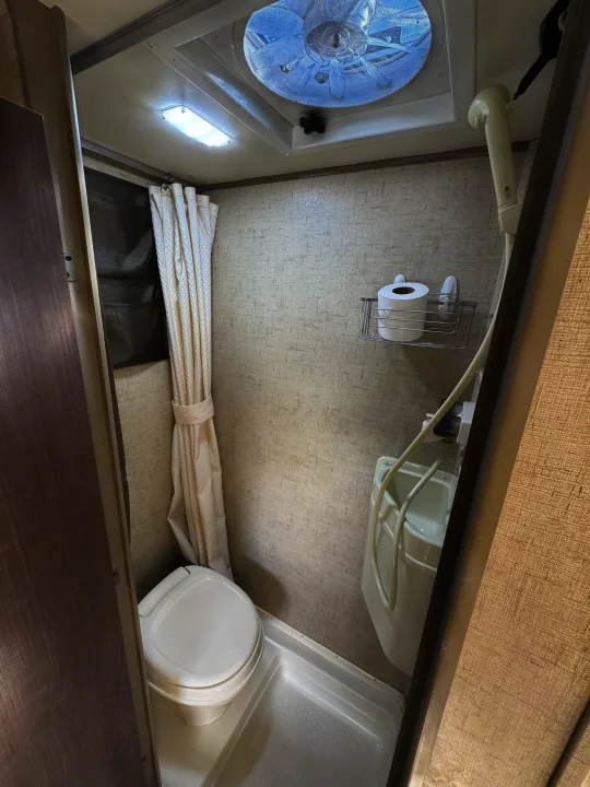 Compact RV rental wet bath featuring a toilet, combined sink/shower, overhead light, and ceiling fan for travel comfort.. R-Pod Hood River Edition 2015